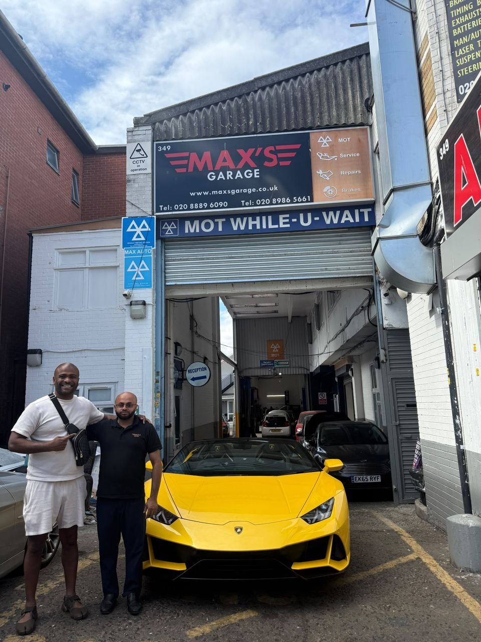 The entrance to Max Autos at 349 High Road, under the blue MOT test station signs, with two men standing beside a yellow sports car.